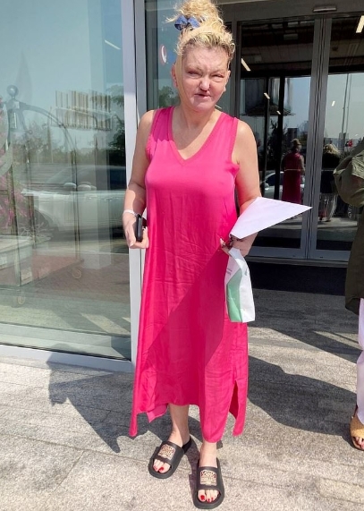 Danniella Westbrook is seen outside a hospital in Dubai with visible facial swelling, wearing a bright pink dress and holding paperwork in a photograph shared on February 10, 2026. | Source: X/DailyMailUK
