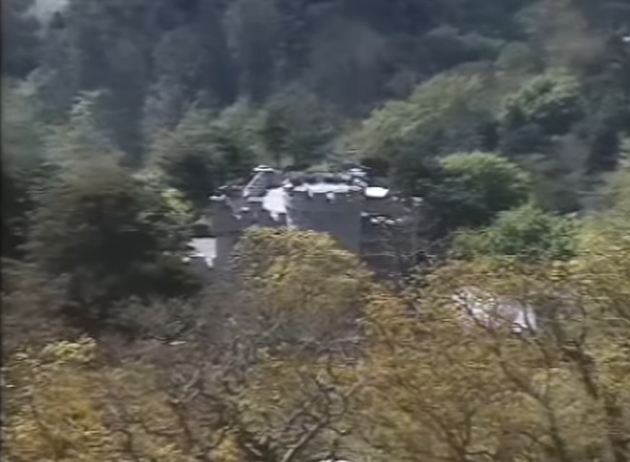 Partially concealed by dense woodland, Ayesha Castle emerges through the trees in this distant view, its pale stone walls blending into the surrounding greenery. The image, taken from a video dated January 26, 2022, captures the secluded positioning of the property, emphasising how thoroughly it is shielded from public view. | Source: YouTube/AndreW