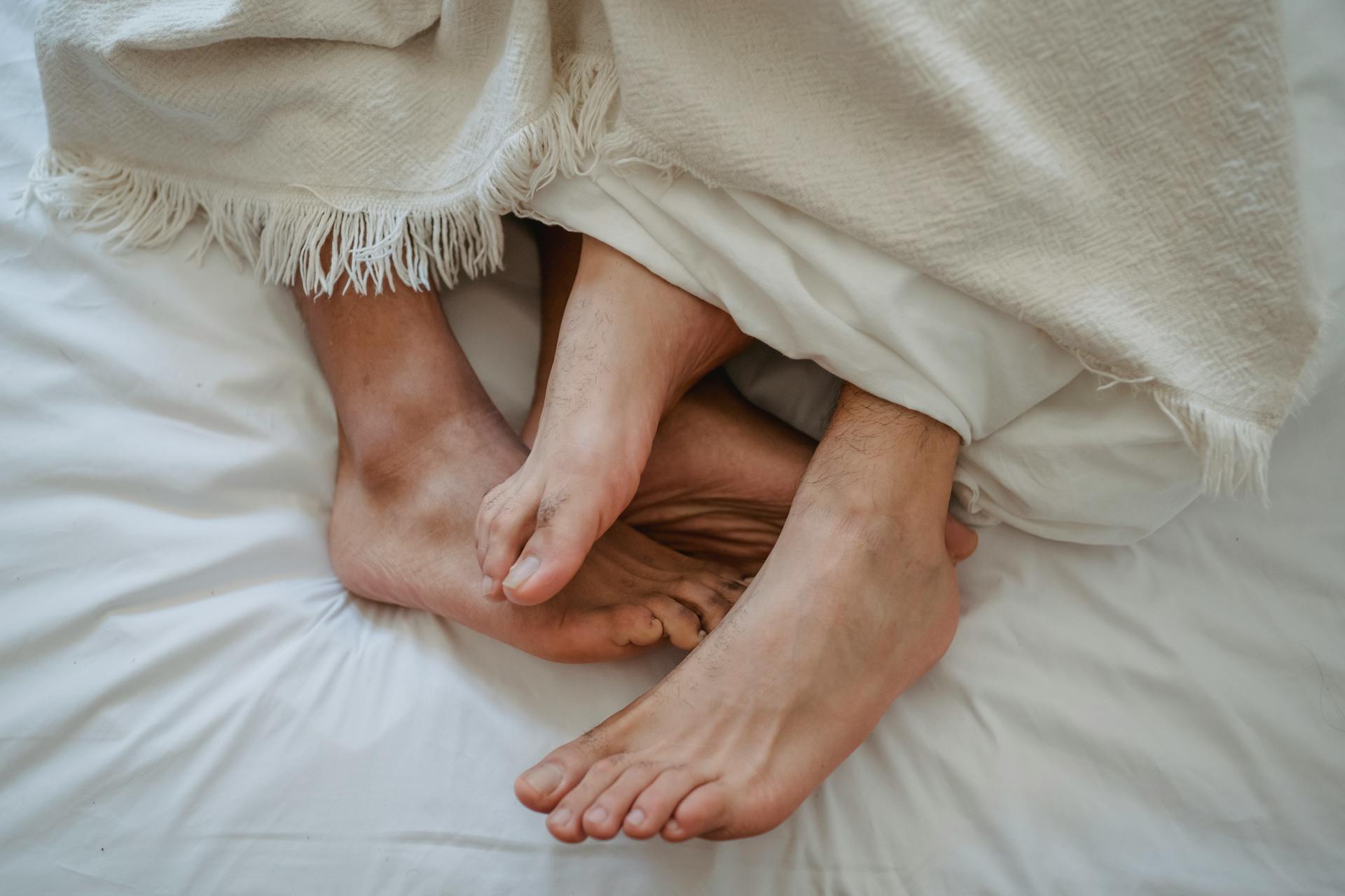 Feet of two men intertwined in bed | Source: Pexels