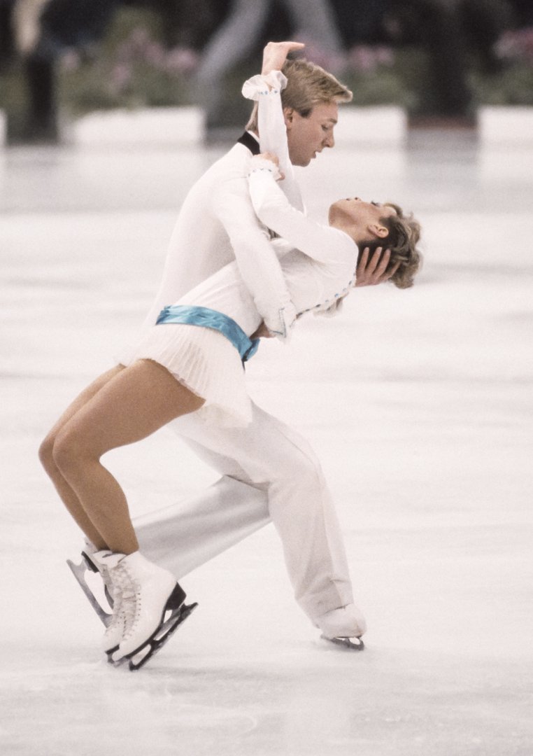 Torvill and Dean execute a dramatic lift during their gold medal-winning Olympic performance. Dean supports Torvill in a sweeping dip, her body arched gracefully as their blades carve a steady curve across the ice.
