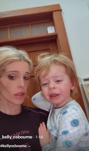 In an earlier clip dated January 14, 2026, Kelly Osbourne holds her son against her shoulder in front of a wooden doorframe, her expression softer and more subdued as she looks directly into the camera. Her son, dressed in patterned pyjamas, appears slightly teary-eyed, clinging to her as if just woken. The unguarded frame captures a rawer side of their morning ritual — less polished and more intimate. | Source: TikTok/_kelly_osbourne