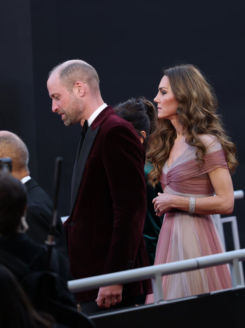In profile, the Prince and Princess of Wales were captured mid-step, their expressions more focused as they progressed towards the auditorium inside the Royal Festival Hall. The Princess's softly draped neckline and statement bracelet caught the light, while the Prince's black lapels sharpened the rich hue of his jacket.