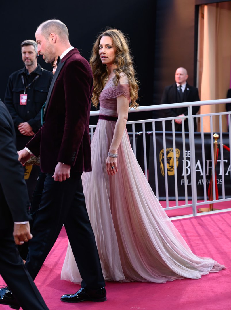 Glancing briefly towards the cameras, the Princess of Wales walked alongside the Prince of Wales as security and event staff lined the perimeter of the pink carpet. The full length of her gown fanned elegantly across the floor, its maroon waistband echoing the Prince's jacket as they continued into the BAFTAs ceremony in London, England.