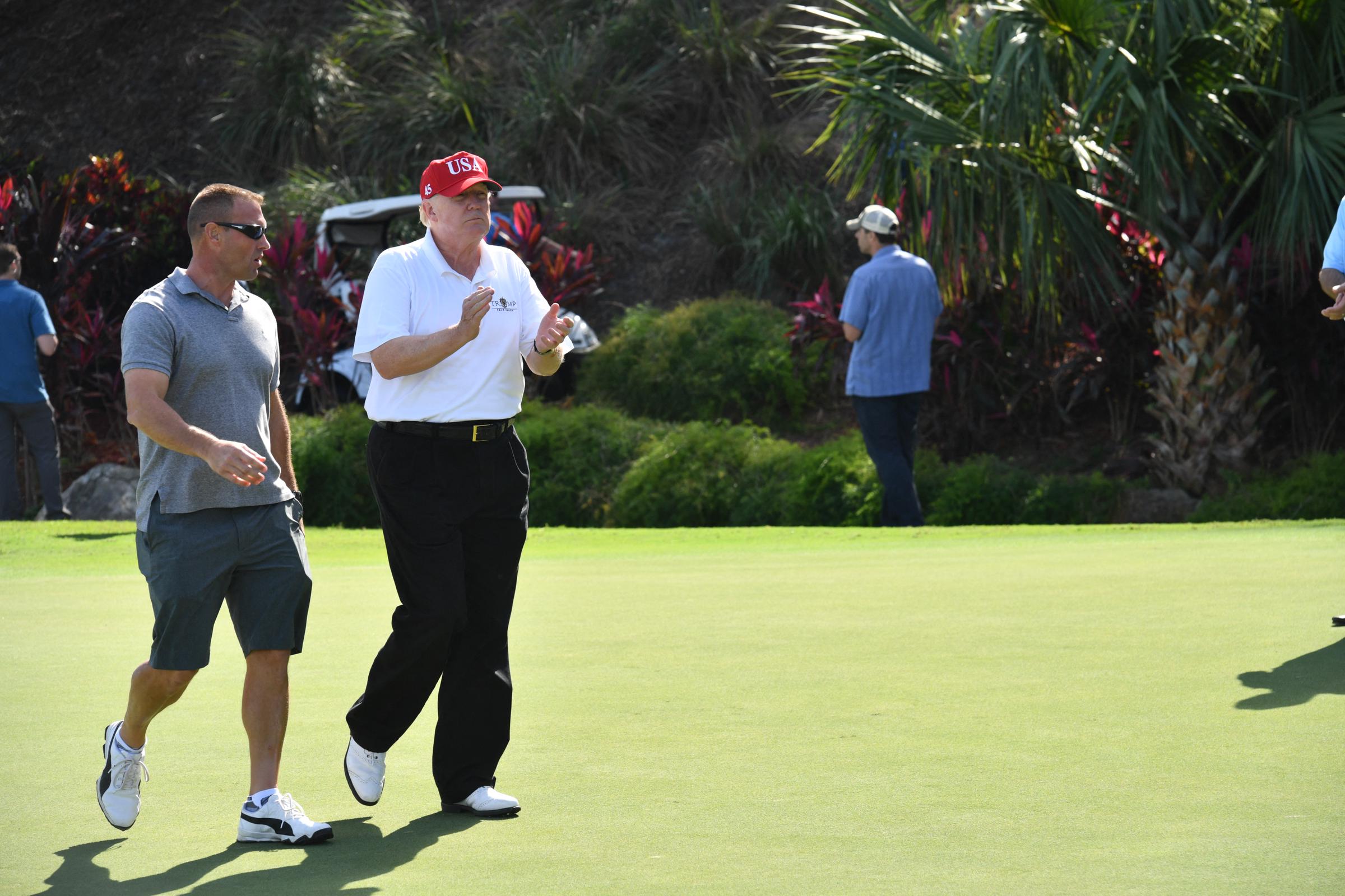 Donald Trump and US Coast Guard Chief Warrant Officer Gene Gibson walk during an invitation for Coast Guard service members to play golf at Trump International Golf Course on December 29, 2017, in Mar-a-Lago, Florida | Source: Getty Images