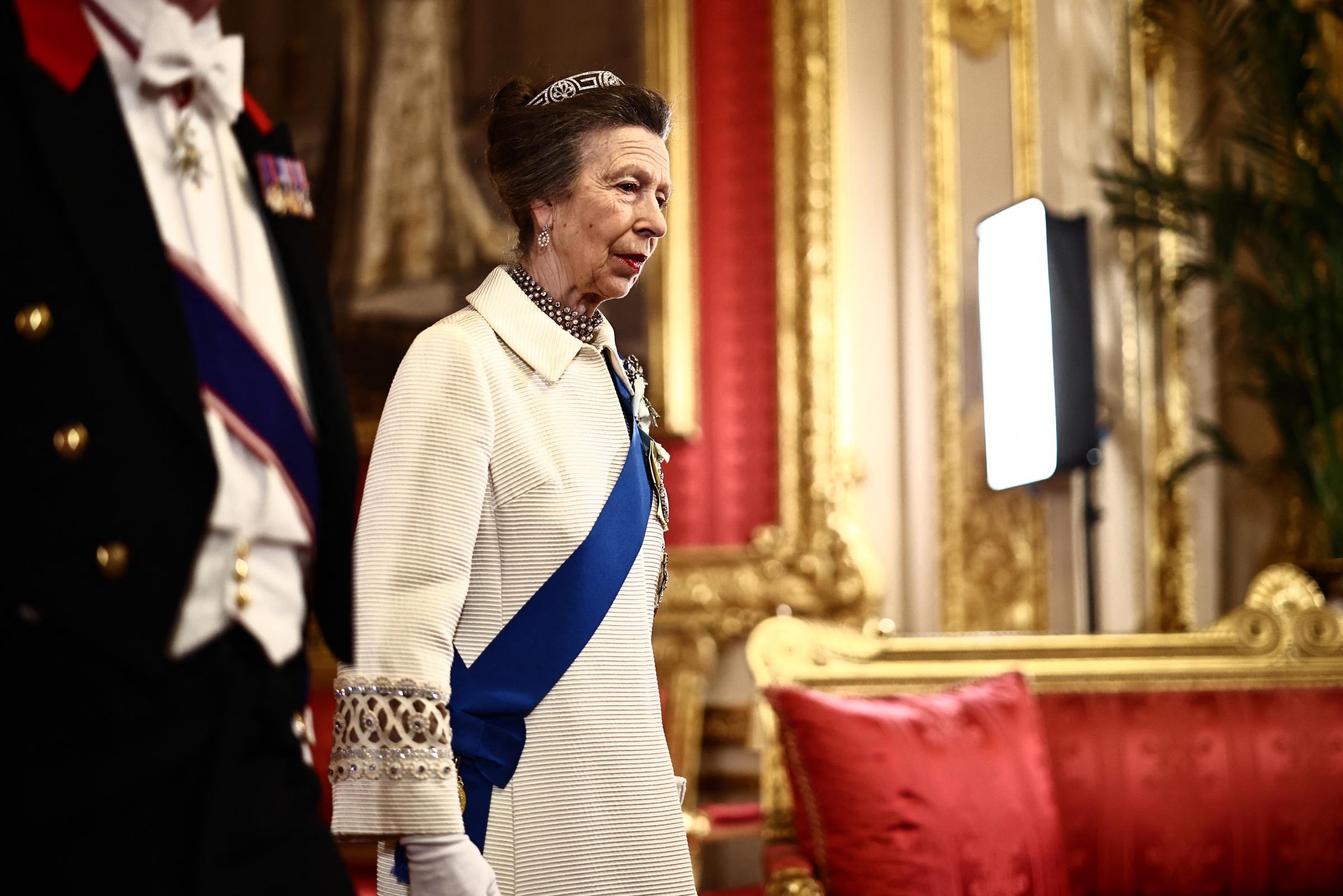 A close-up view of Princess Anne as she arrives at St George's Hall, capturing the coat's most talked-about surviving detail — the intricate geometric circular trim on the cuffs, unchanged after 57 years. Her tiara, drop earrings, and multi-strand pearl necklace frame the updated plain collar.