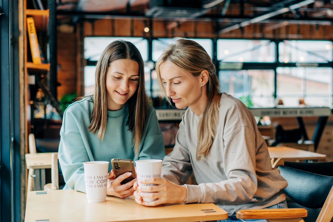 Two cheerful smiling women are watching social networks in a mobile phone | Source: Getty Images