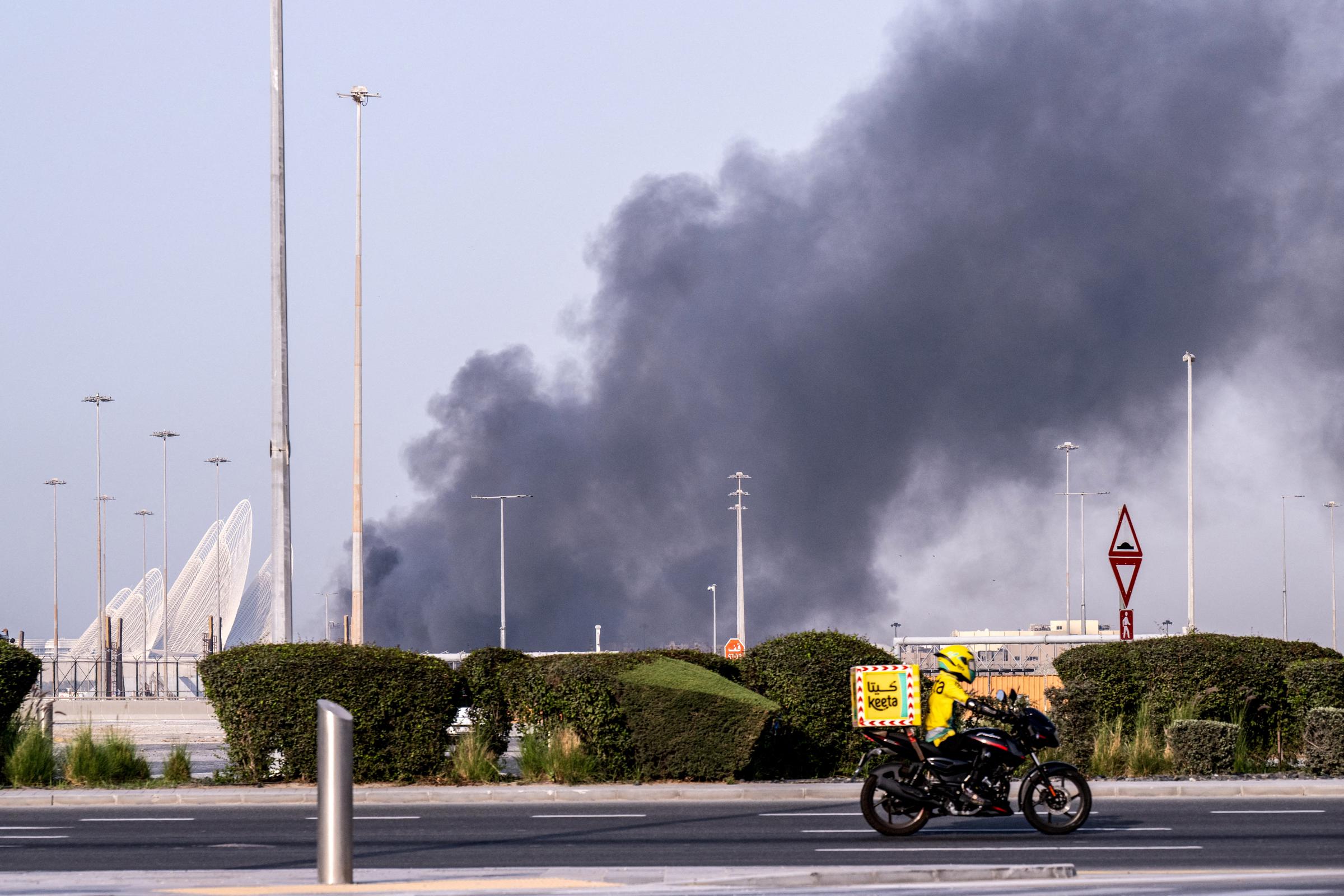 A food delivery bike drive close to a plume of smoke rising from the Zayed Port following a reported Iranian strike in Abu Dhabi on 1 March 2026. | Source: Getty Images