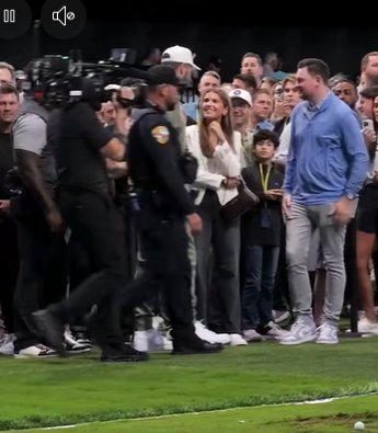 Travis Kelce, dressed in a white cap, olive-green tracksuit, and white sneakers, stops by the crowd barrier to greet fans, chatting with a smiling Kai Trump as security and onlookers gather around. | Source: Facebook/PageSix