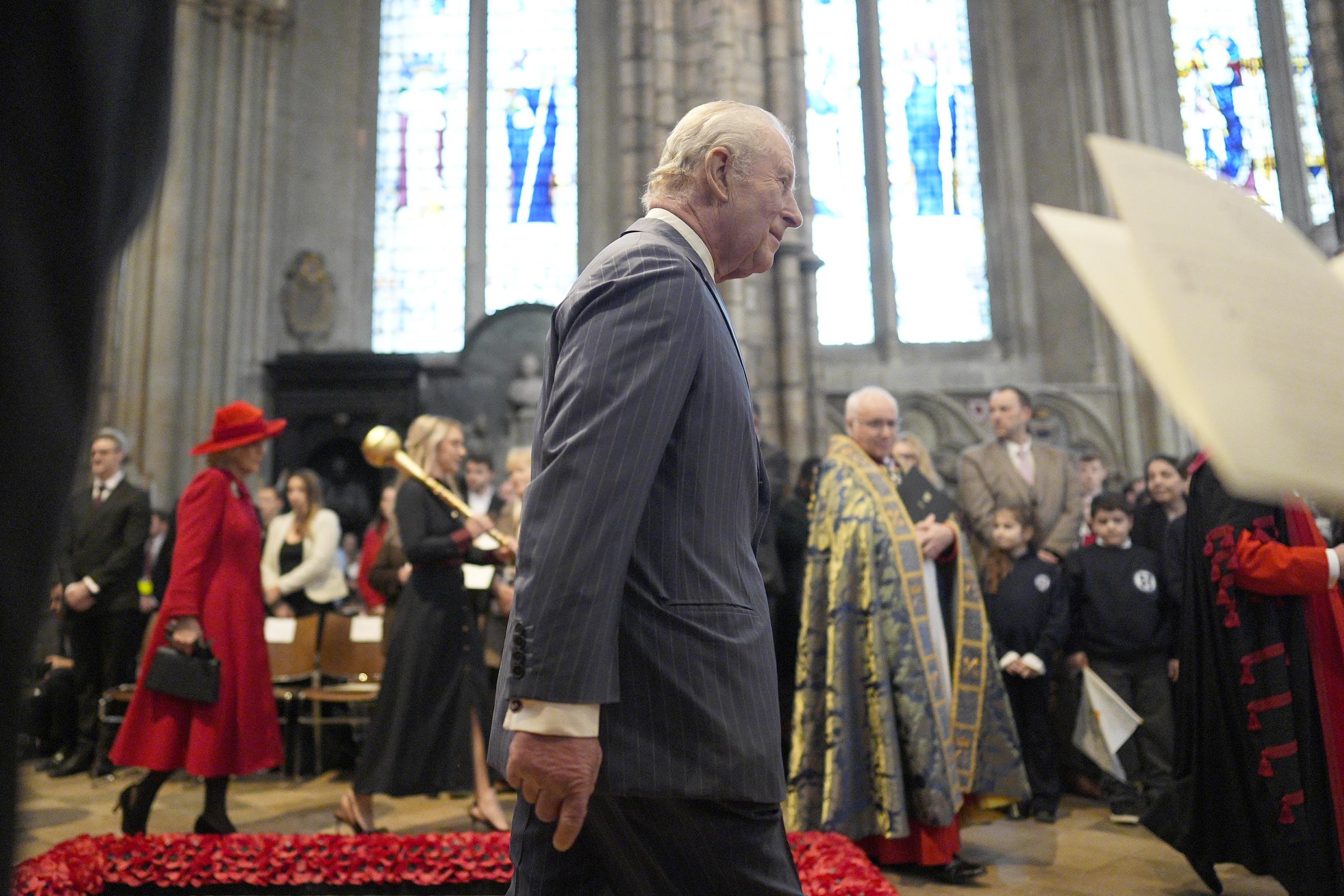 King Charles III processed through the nave of Westminster Abbey in his navy pinstripe suit, the congregation rising on either side as a clergy member in gold vestments led the way, Queen Camilla's red coat a vivid presence in the background, beneath the Abbey's towering stained-glass windows on 9 March 2026.