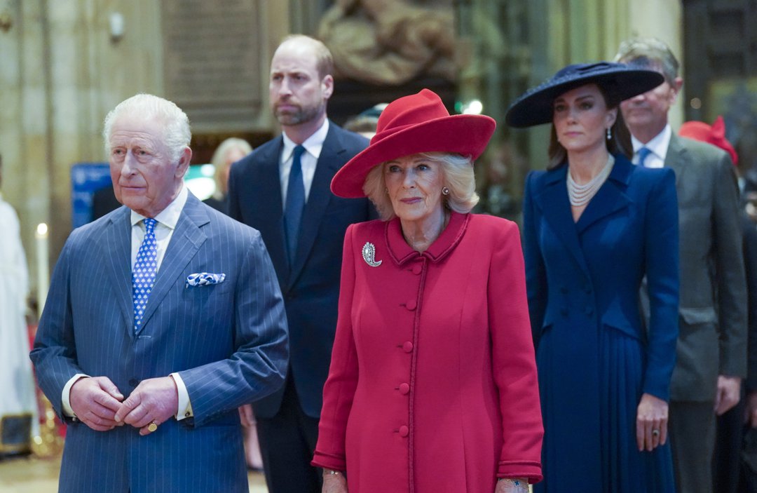 King Charles III and Queen Camilla stood at the front of the procession inside Westminster Abbey on 9 March 2026, the King's hands clasped calmly at his waist and the Queen's diamond brooch gleaming against her vivid red coat, while the Prince of Wales and the Princess of Wales, her layered pearl necklace catching the light beneath her wide navy hat, followed closely and purposefully behind them as a family.