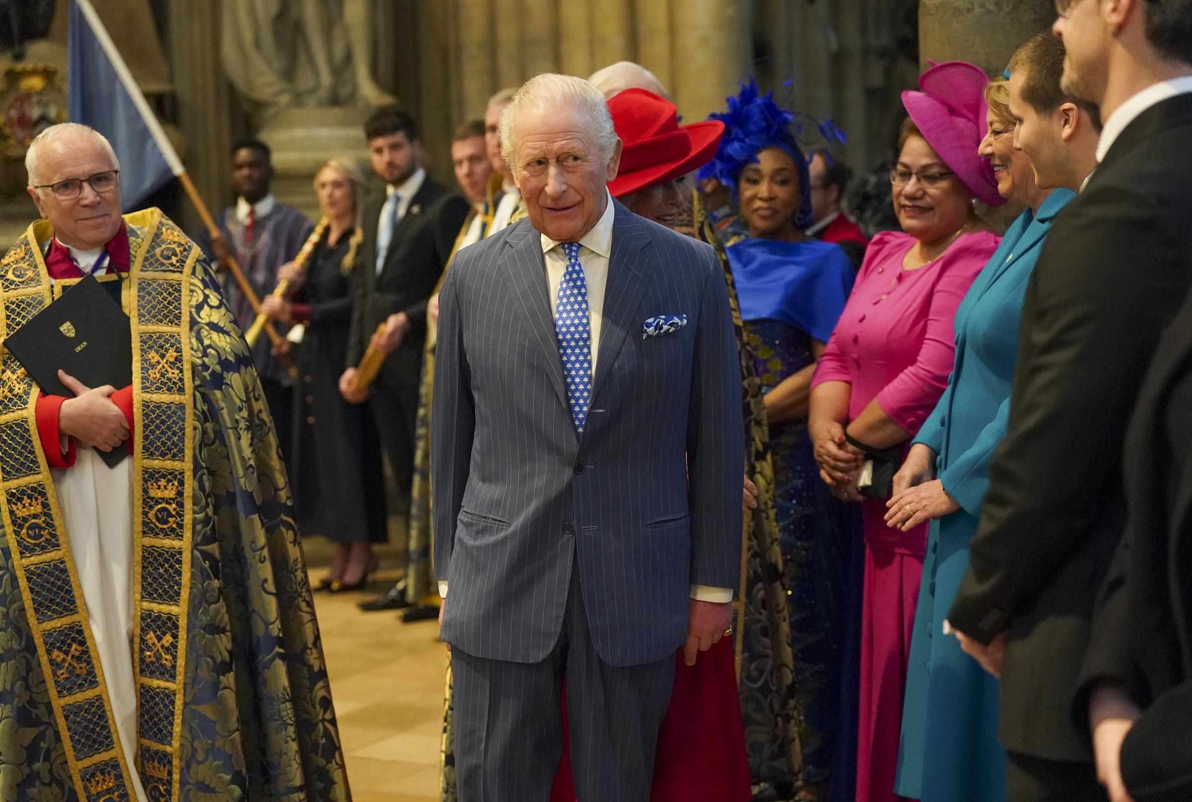 King Charles III walked the central aisle of Westminster Abbey on 9 March 2026, led by a clergyman in embroidered gold and navy vestments, as a vivid line of Commonwealth dignitaries dressed in jewel-bright shades of cobalt blue, fuchsia, and teal lined up on either side to greet him, with Queen Camilla's distinctive red wide-brimmed hat a striking flash of colour just visible behind him.