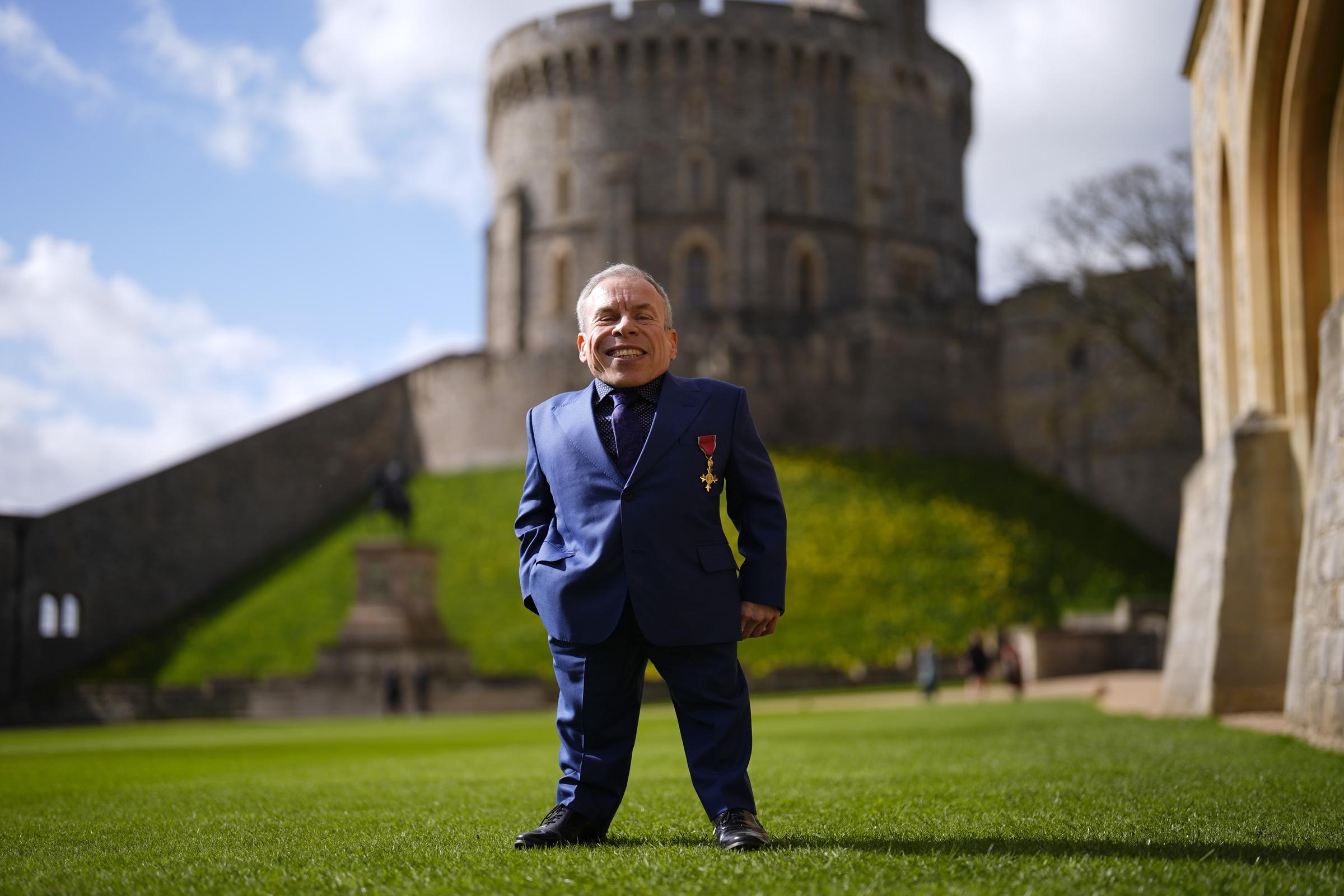 Warwick Davis stands on the castle grounds with a satisfied smile, the ancient stonework of Windsor's Round Tower looming large behind him &mdash; a striking image of a man very much at ease with the extraordinary. Named on King Charles III's New Year's Honours list for 2026 alongside Idris Elba and Cynthia Erivo, the 56-year-old actor was recognised on the day for his outstanding services to both drama and charity.
