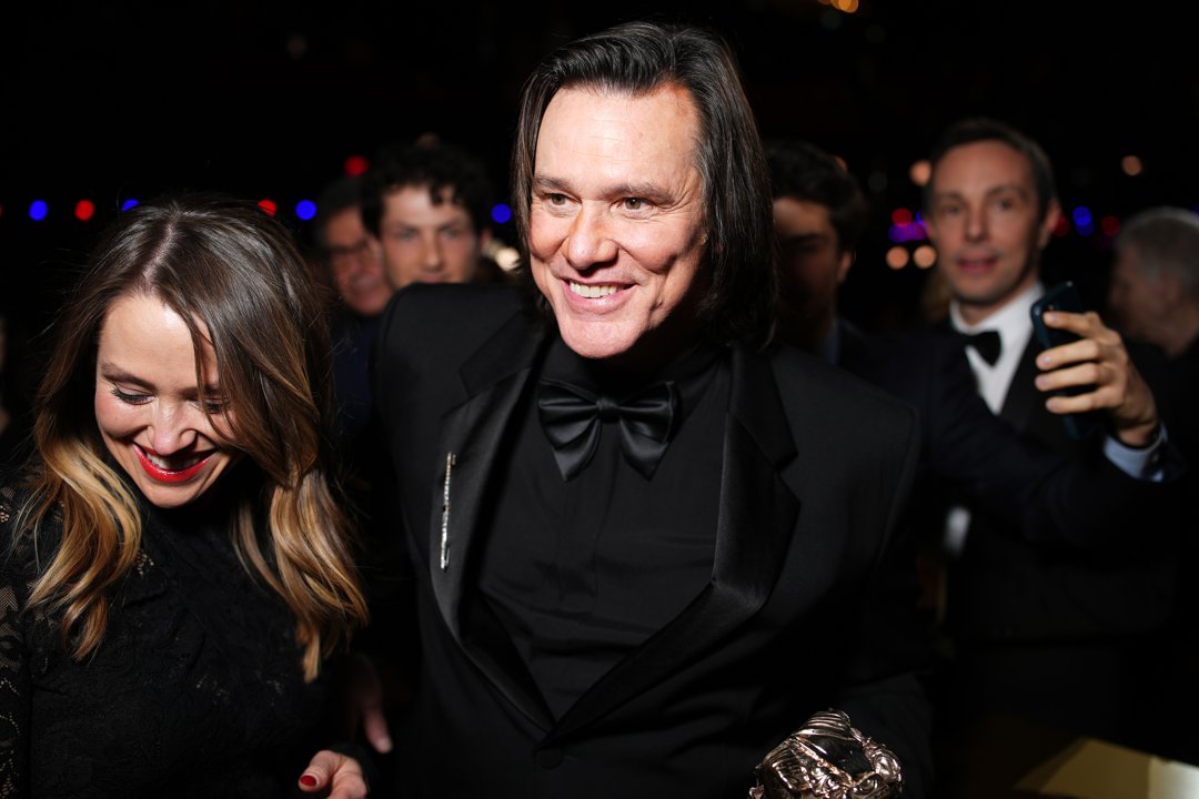 Smiling beside Jane Erin Carrey, Jim Carrey cuts a polished figure in a classic black tuxedo. The actor clutches his C&eacute;sar Award as camera flashes and onlookers crowd in around them.