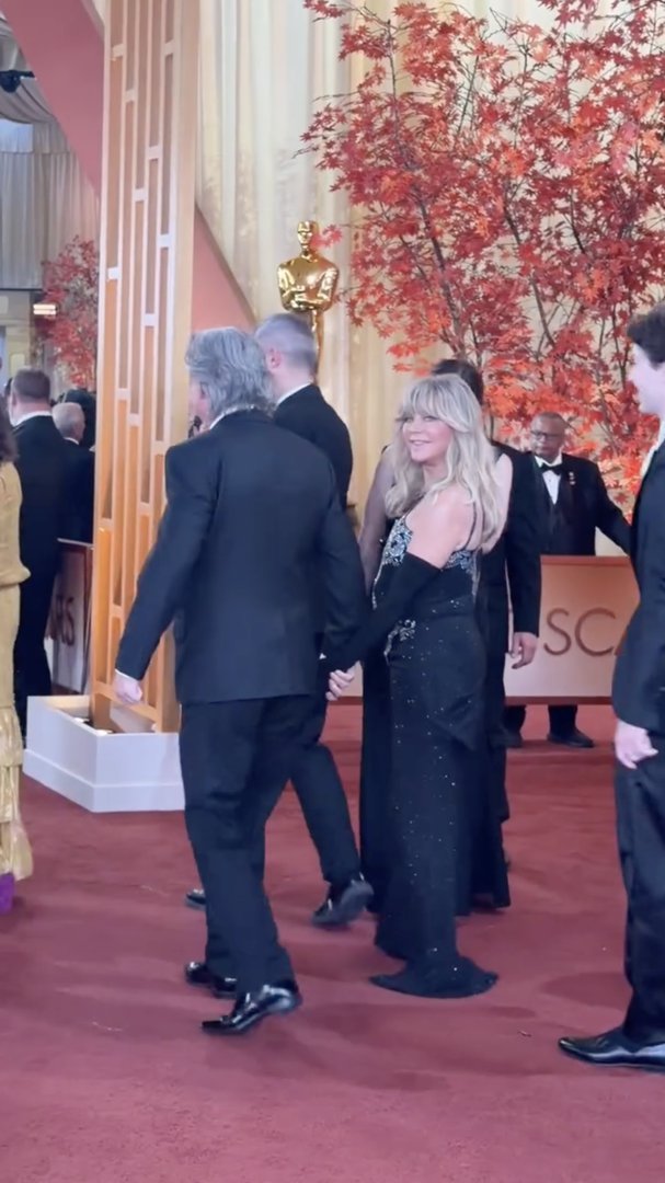 Goldie Hawn continues down the red carpet behind Kurt Russell, her black gown shimmering under bright lights as fans and media capture the moment. | Source: Instagram/enews