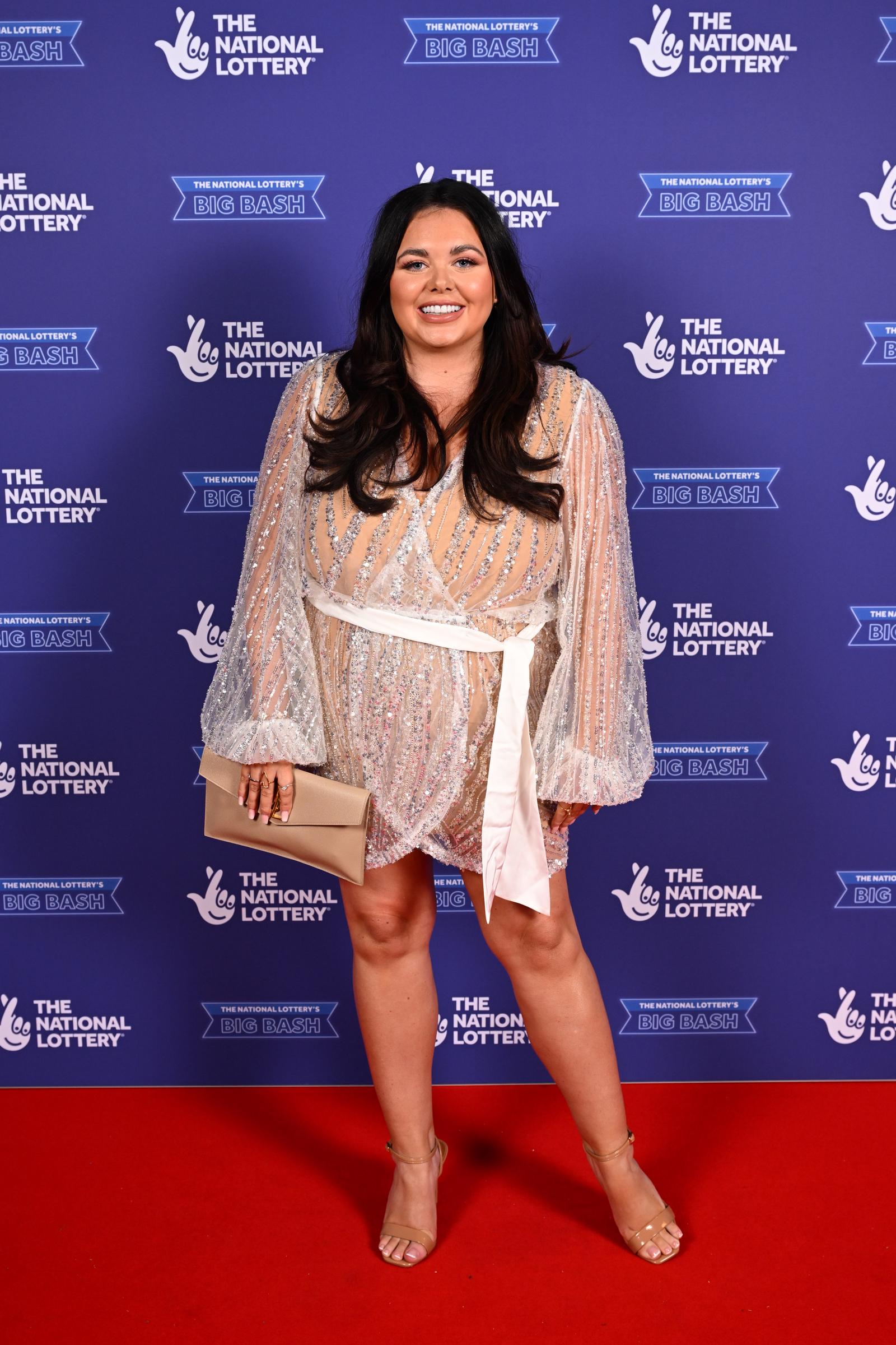 Moffatt glittered on the red carpet at the National Lottery's Big Bash at OVO Arena Wembley in a sheer, embellished wrap mini dress with voluminous long sleeves and a white sash tie at the waist, completing the look with strappy gold heels and a gold clutch.